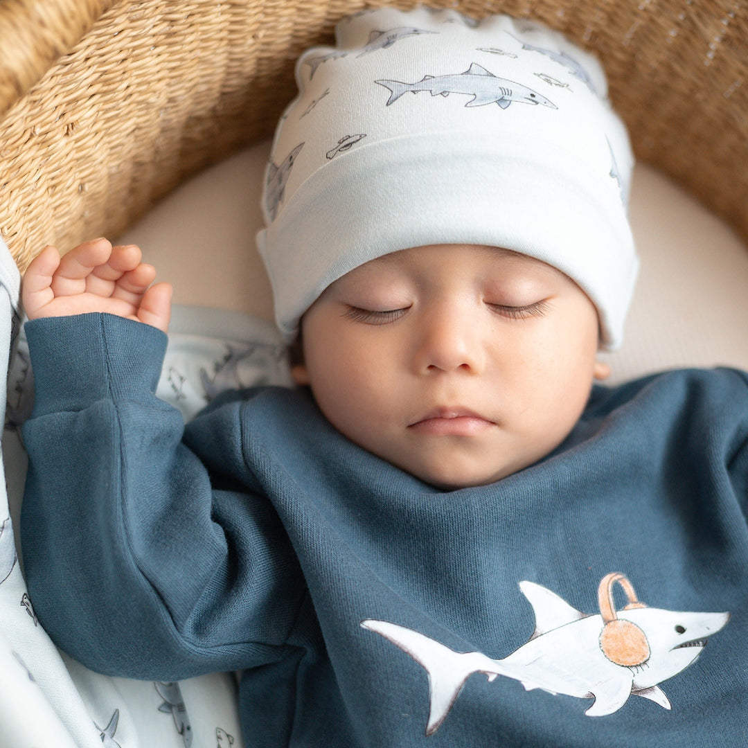 Child wearing sweatshirt and hat with shark pattern.