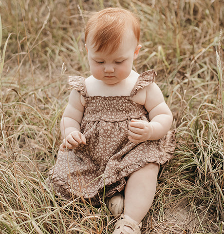 A child wearing an Organic Printed Smocked Summer Dress in Latte Floral from The Neutral Collection.