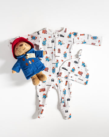 Baby onesie with Paddington Bear design, matching hat, and plush toy on a white background