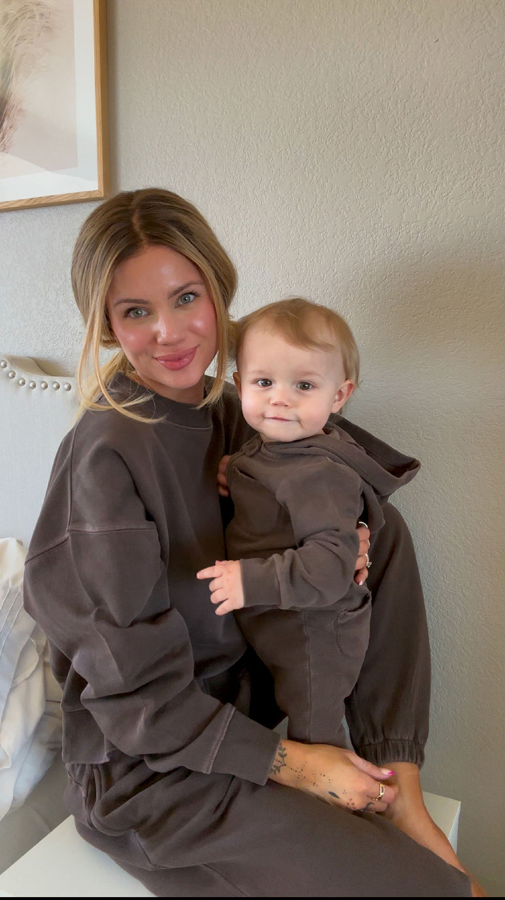 Woman holding a baby both wearing matching brown outfits indoors.