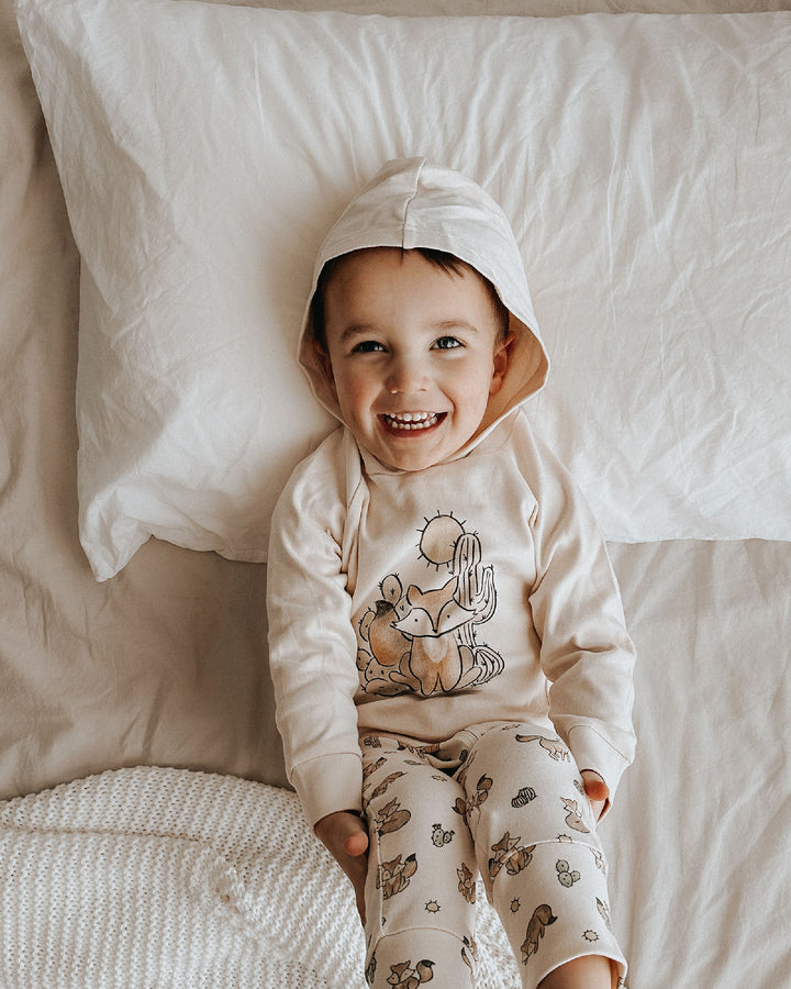 Child wearing a hoodie and pajama set with animal designs on a bed.