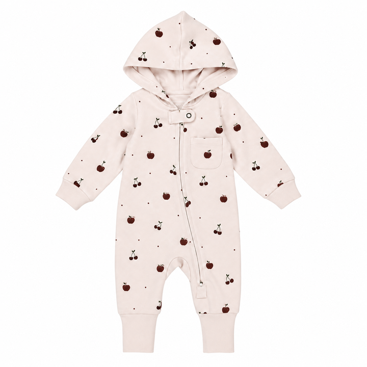 A baby hooded one-piece romper in a very pale blush pink, featuring a small all-over print of dark red cherries and tiny black dots, with a snap-button front and a chest pocket.