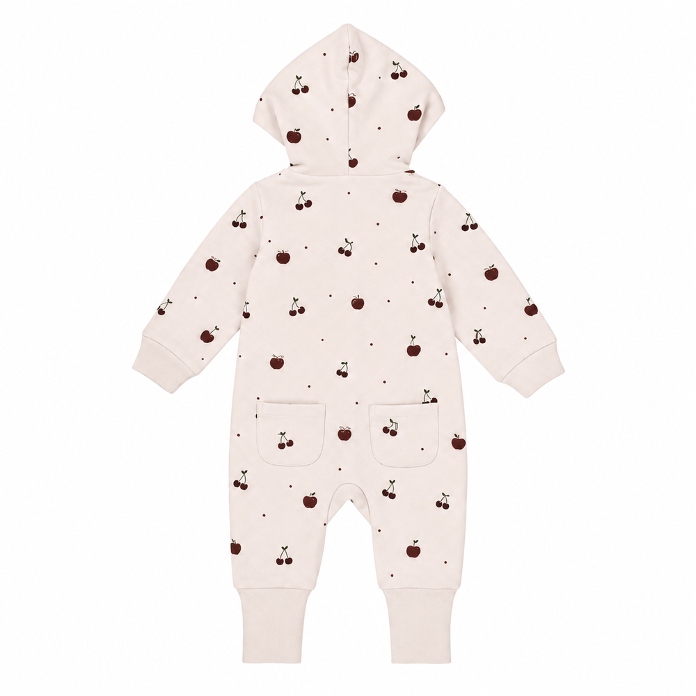 A baby hooded one-piece romper in a warm off-white/cream color, decorated with a small all-over print of dark brown cherries and tiny dark dots. The romper features long sleeves, ribbed cuffs, and two front patch pockets.