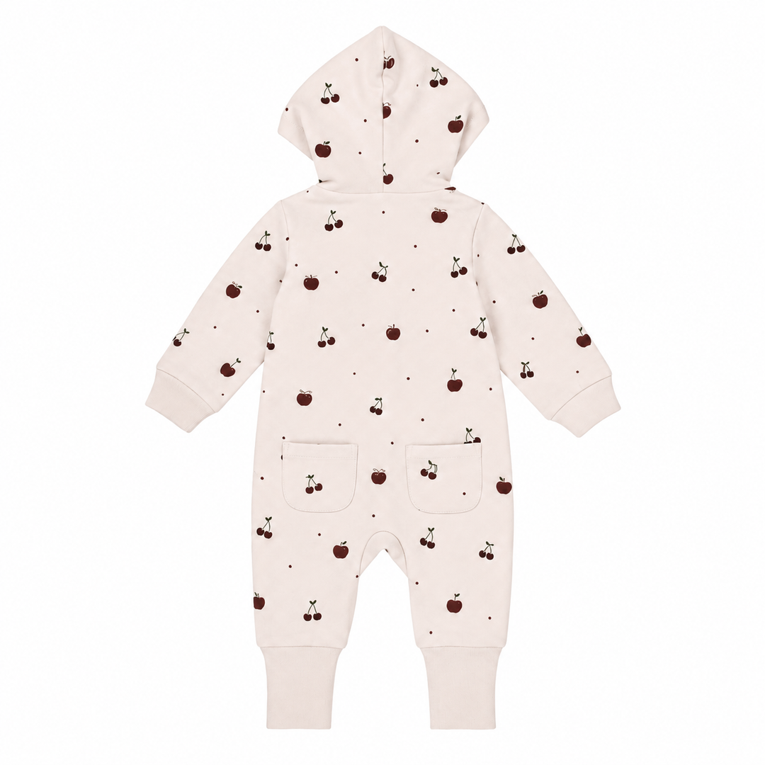 A baby hooded one-piece romper in a warm off-white/cream color, decorated with a small all-over print of dark brown cherries and tiny dark dots. The romper features long sleeves, ribbed cuffs, and two front patch pockets.