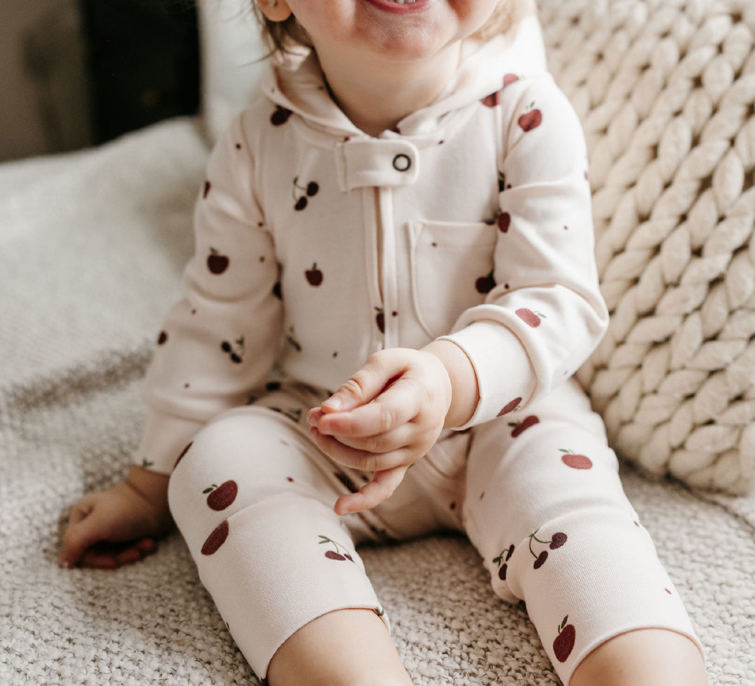 Child wearing Organic Hooded Zipper Romper in Cherry Apple.