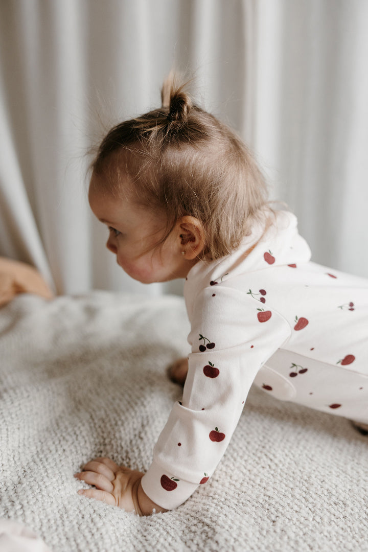 Child wearing Organic Hooded Zipper Romper in Cherry Apple.