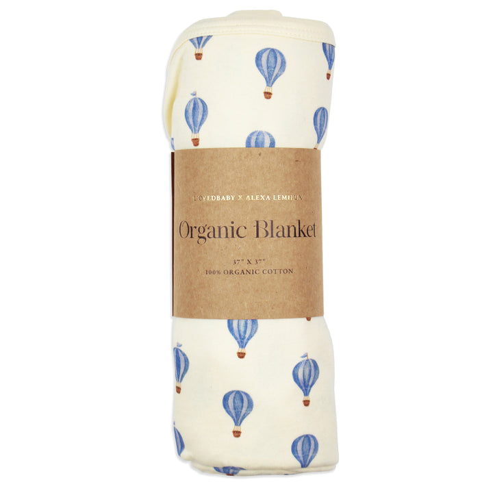 flat image of swaddle blanket in blue hot air balloon print, rolled neatly and placed inside kraft color card stock wrap sleeve