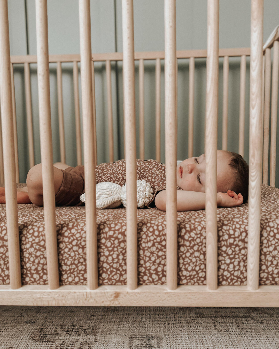 Child sleeping in crib. Mattress in the crib is fitted with our crib sheet in the Latte Floral color option.