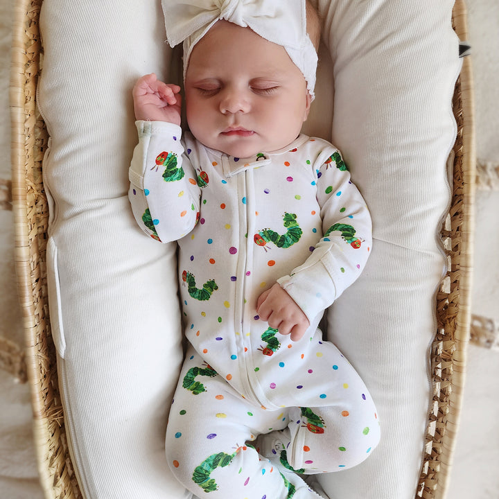 image of baby girl sleeping in basket, wearing the caterpillar print zipper footie and solid white headband