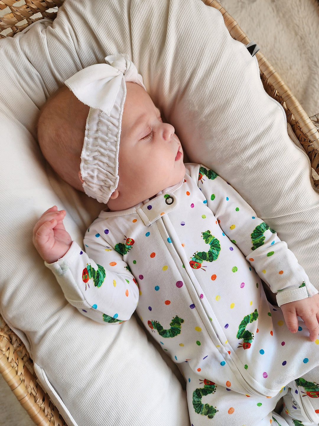 close up image of baby girl sleeping in basket, wearing the caterpillar print zipper footie and solid white headband