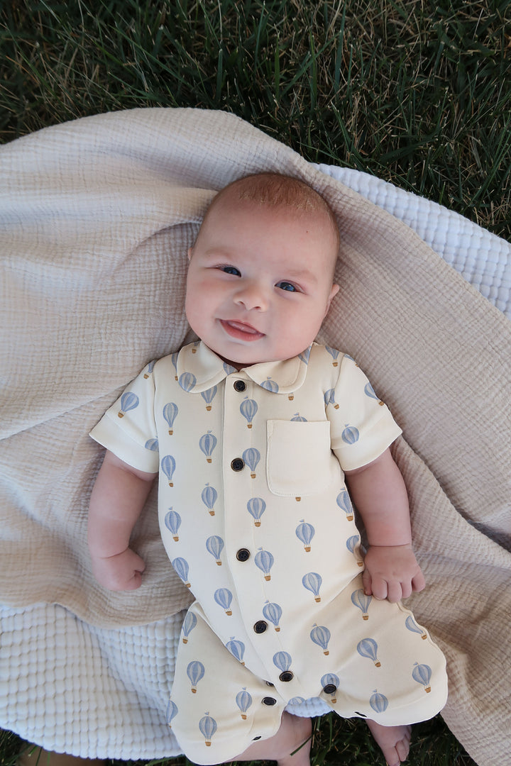 Baby wearing a patterned outfit lying on a blanket outdoors