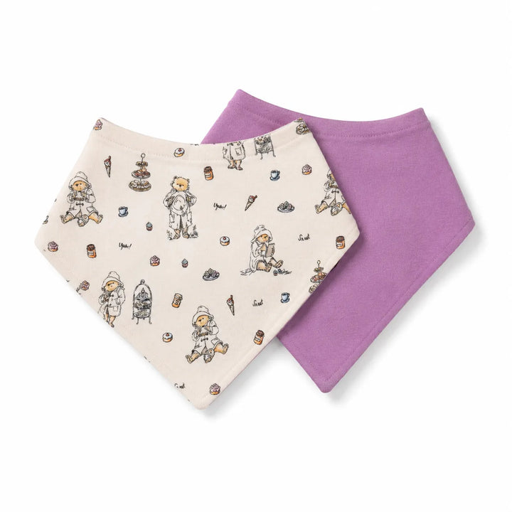Two baby bandana bibs, one in cream with a cute astronaut and food-themed print, and one in solid lavender purple, displayed on a clean white background.