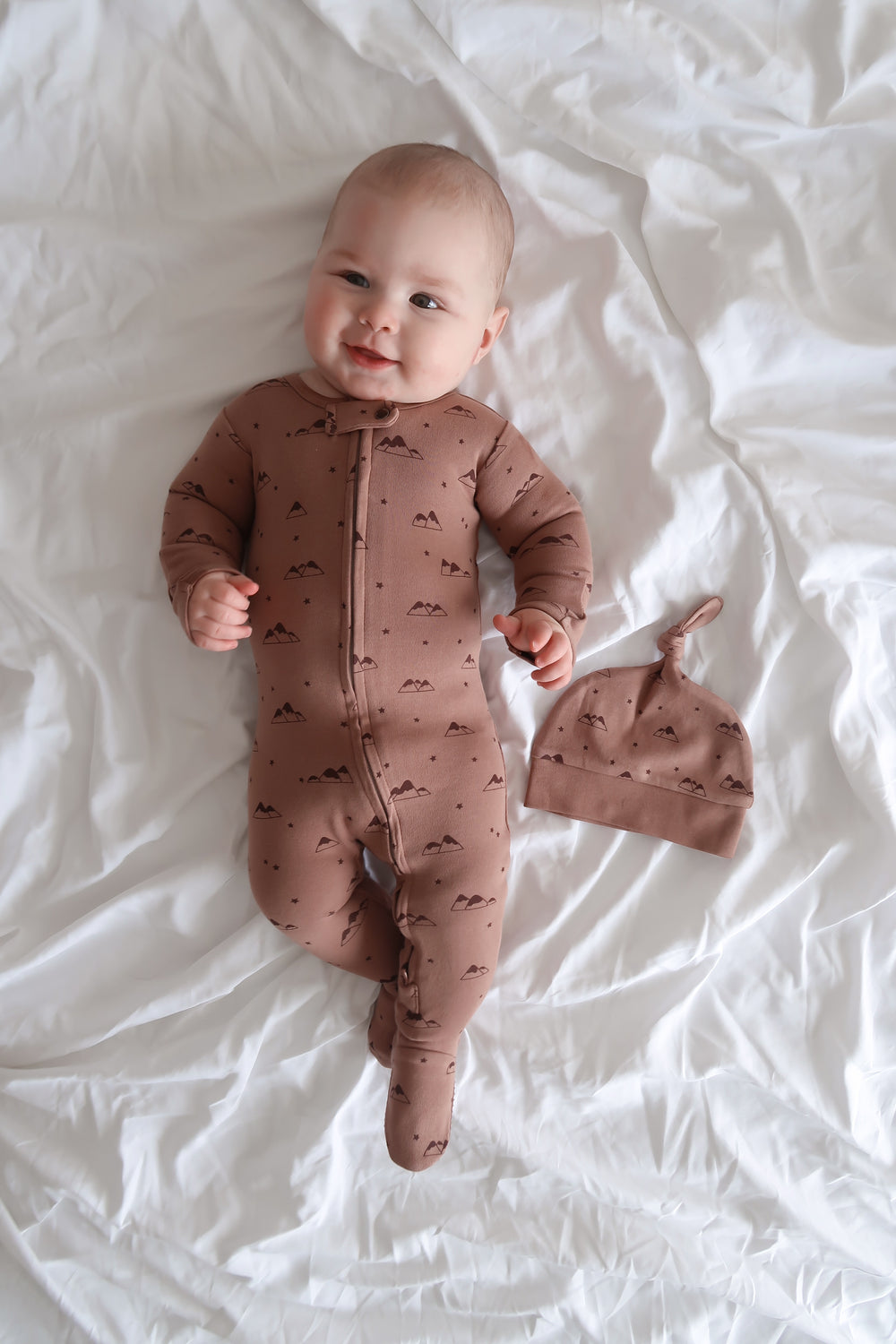 Baby in a brown onesie with a matching hat on a white surface