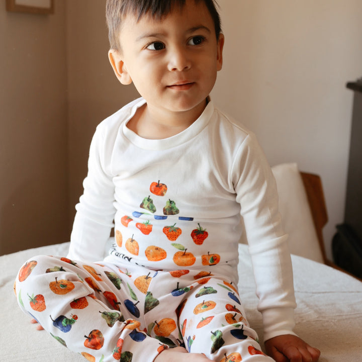 image of boy sitting on bed wearing kids pj set in "still hungry" print from very hungry caterpillar collection