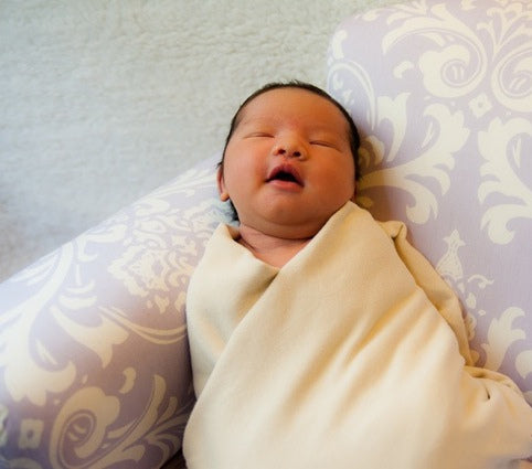 Child wearing Organic Swaddling Blanket in Buttercream.