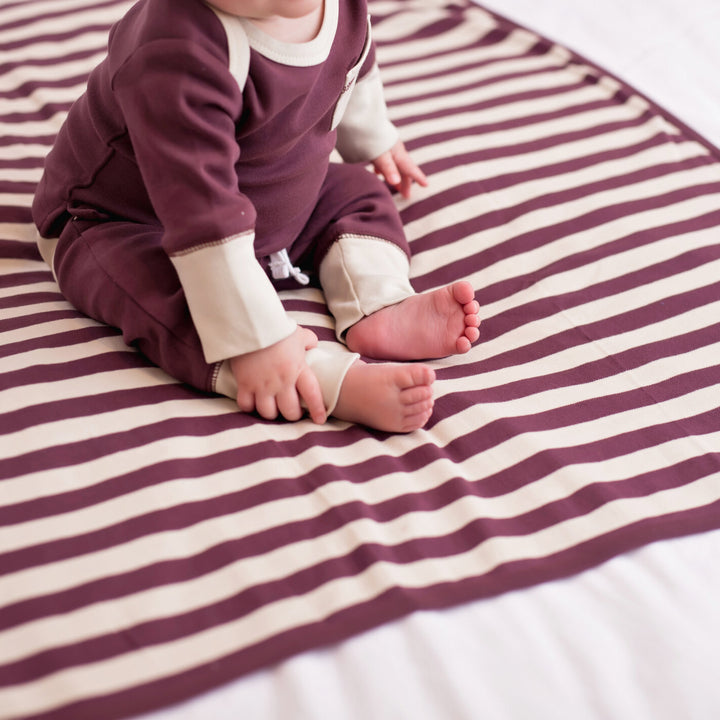 Child wearing Organic Swaddling Blanket in Eggplant/Stone Stripe.