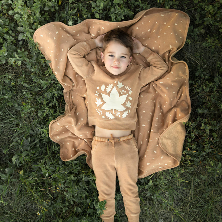 Child wearing Organic Cozy Blanket in Toffee Leaf.