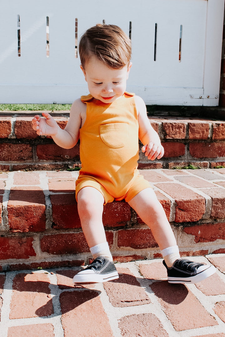 Child wearing Organic Kids' Sleeveless Romper in Tangerine.