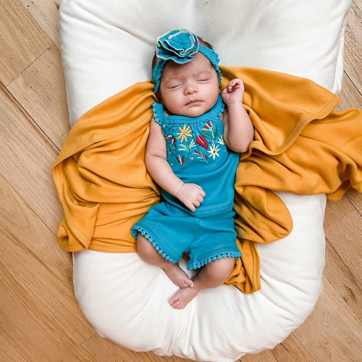 Child wearing Organic Swaddling Blanket in Tangerine.